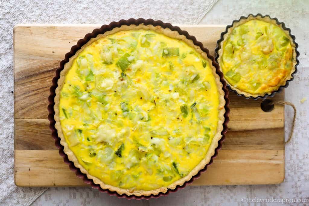 A large leek and gruyere quiche and a small leek and gruyere tartlet on a wooden board.