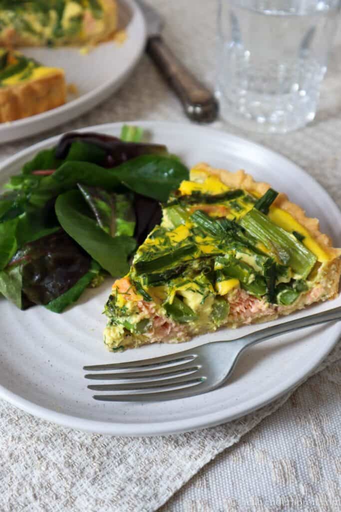 Slice of asparagus and salmon quiche on a plate with a green salad.