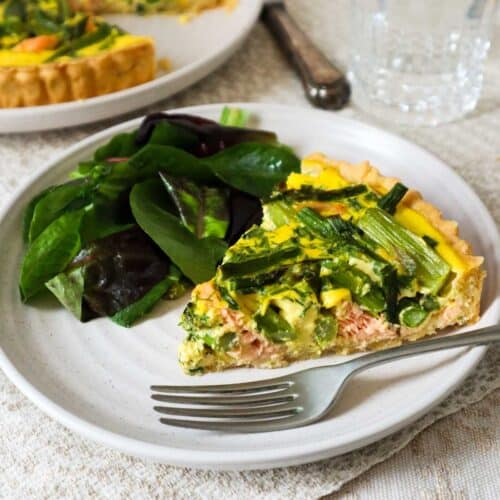 Slice of asparagus and salmon quiche on a plate with a green salad.