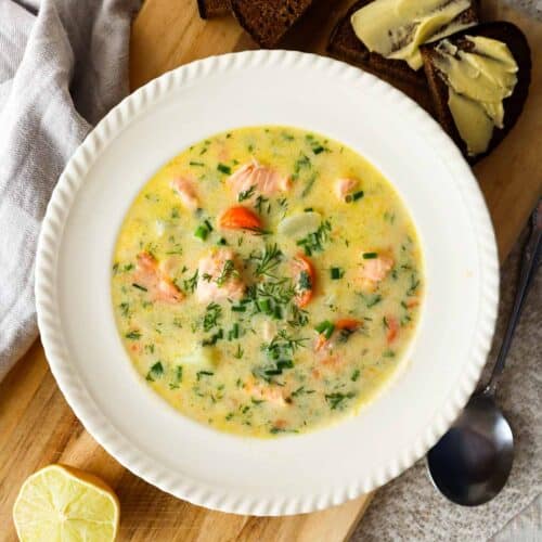 Creamy salmon soup in a beige bowl served with dark rye bread and butter on a wooden board.