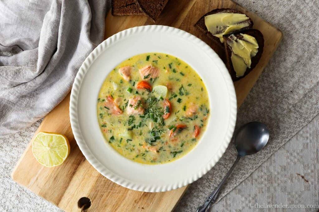 Latvian salmon soup served with dark rye bread and butter on a wooden board.