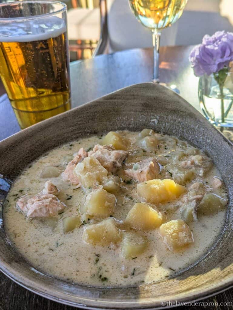 Finnish lohikeitto in Helsinki served in a bowl with a glass of beer showing chunks of potatoes and salmon.