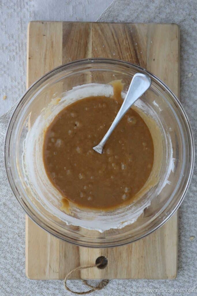 A smooth mixture of flour, baking soda, melted butter, brown sugar, white sugar and vanilla in a glass bowl.