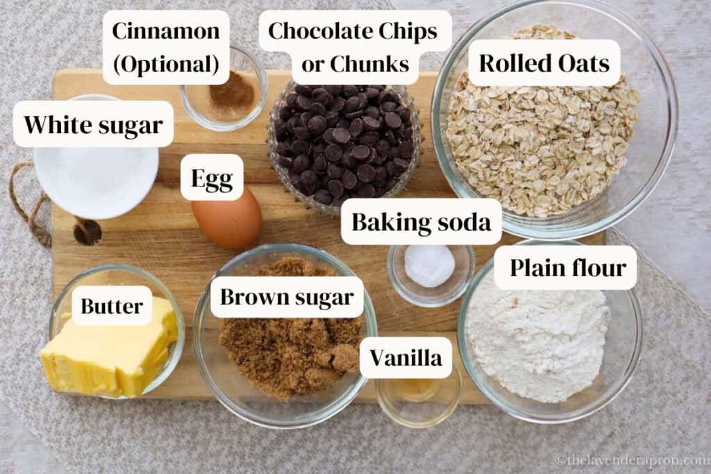 Ingredients to make oatmeal chocolate chip cookies including oats, chocolate chips, vanilla, brown and white sugar, butter and an egg.