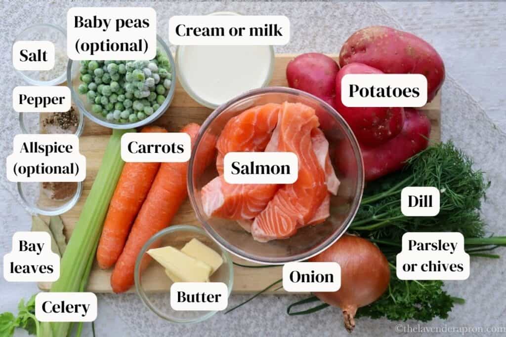 Salmon, potatoes, carrots, onion, celery, dill, salt, pepper, bay leaves, allspice, peas and cream on a wooden board.
