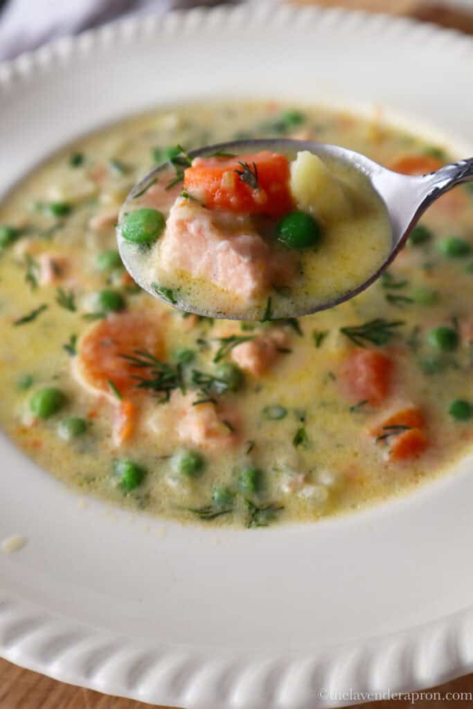 Spoonful of creamy salmon soup with salmon, potato, carrot and peas showing.