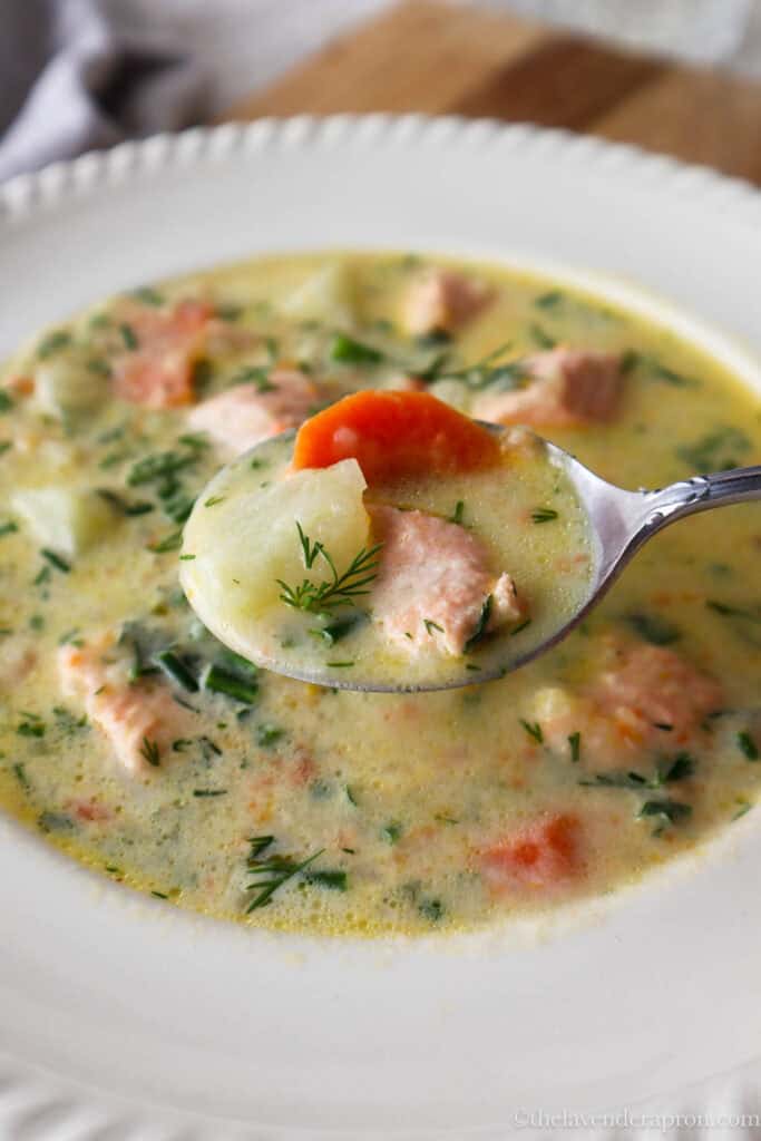 Spoonful of creamy salmon soup showing a piece of potato, salmon, carrot and dill.
