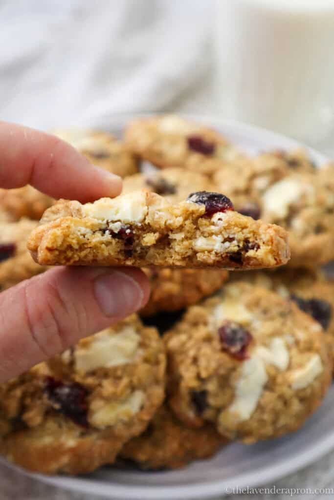 Hand holding a white chocolate and cranberry oat cookie with a bite taken out of it showing a chewy center.