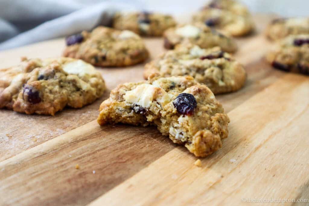 Oatmeal white chocolate cranberry cookies on a wooden board with one cookie showing a chewy center.