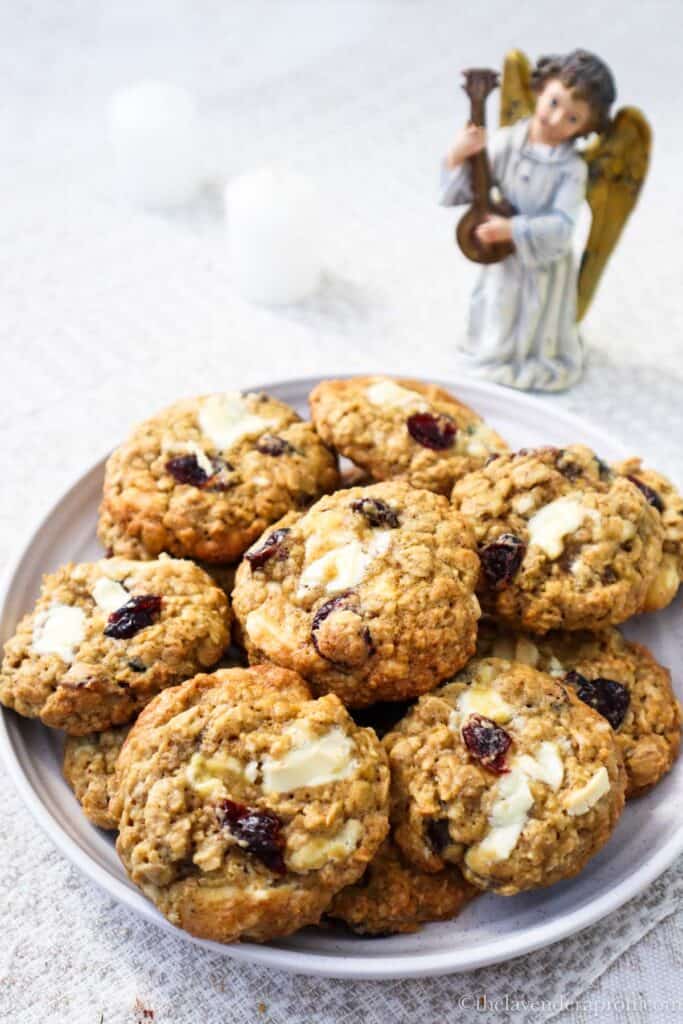 Oatmeal cranberry white chocolate cookies on a plate with a Christmas angel and candles.